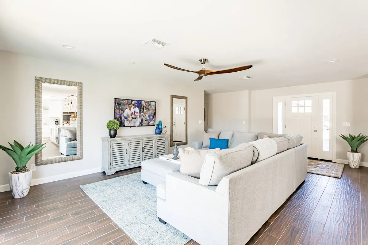 A spacious living room features a large sectional sofa positioned to face a wall-mounted TV, with a decorative mirror and an entrance door adding style and light. The cozy yet modern furnishings foster a relaxed, communal atmosphere ideal for movie marathons, game nights, or unwinding after a day of adventure.