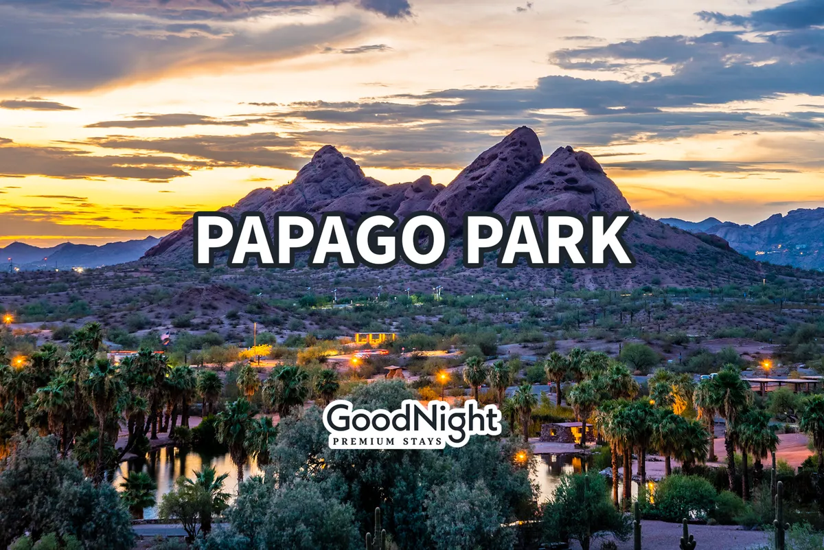A serene view of Papago Park featuring reddish mountains, palm trees, and a shimmering lake. The landscape is tranquil and natural, evoking the spirit of outdoor exploration and picnicking.
