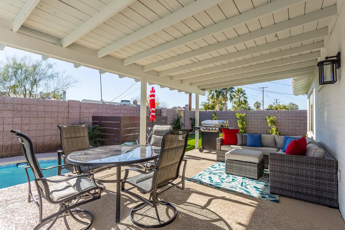 A relaxed poolside setting with a rectangular swimming pool, a shaded outdoor seating area, dining table, and a BBQ grill. The arrangement encourages both poolside relaxation and outdoor meals, with lush greenery adding to the sense of privacy and comfort.