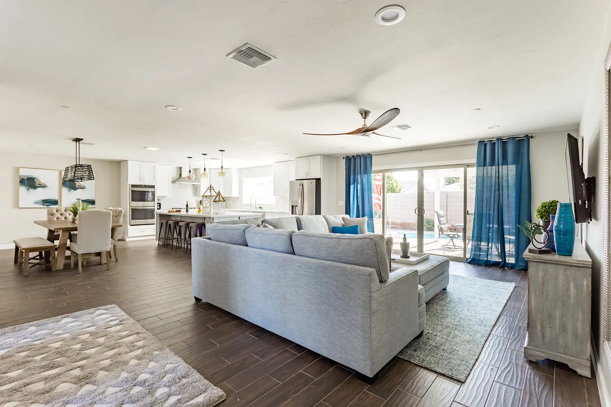 A spacious, open-concept living area with a comfortable sofa, dining table, kitchen island, and sliding glass doors leading outside. The layout encourages gatherings and offers seamless indoor-outdoor living.