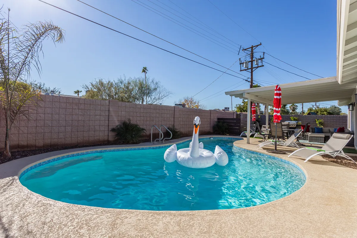 This exterior image captures a sunny pool area with an inviting swimming pool, an inflatable swan, and a comfortable patio space. The scene emphasizes outdoor family fun, relaxation, and playful moments at home.