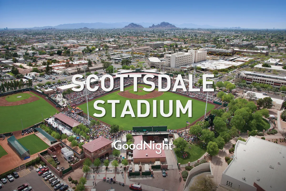 A lively exterior image of Scottsdale Stadium, featuring a bustling baseball field, a crowd of engaged spectators, and scenic mountain views in the background. The image radiates energy and highlights a popular local event venue.