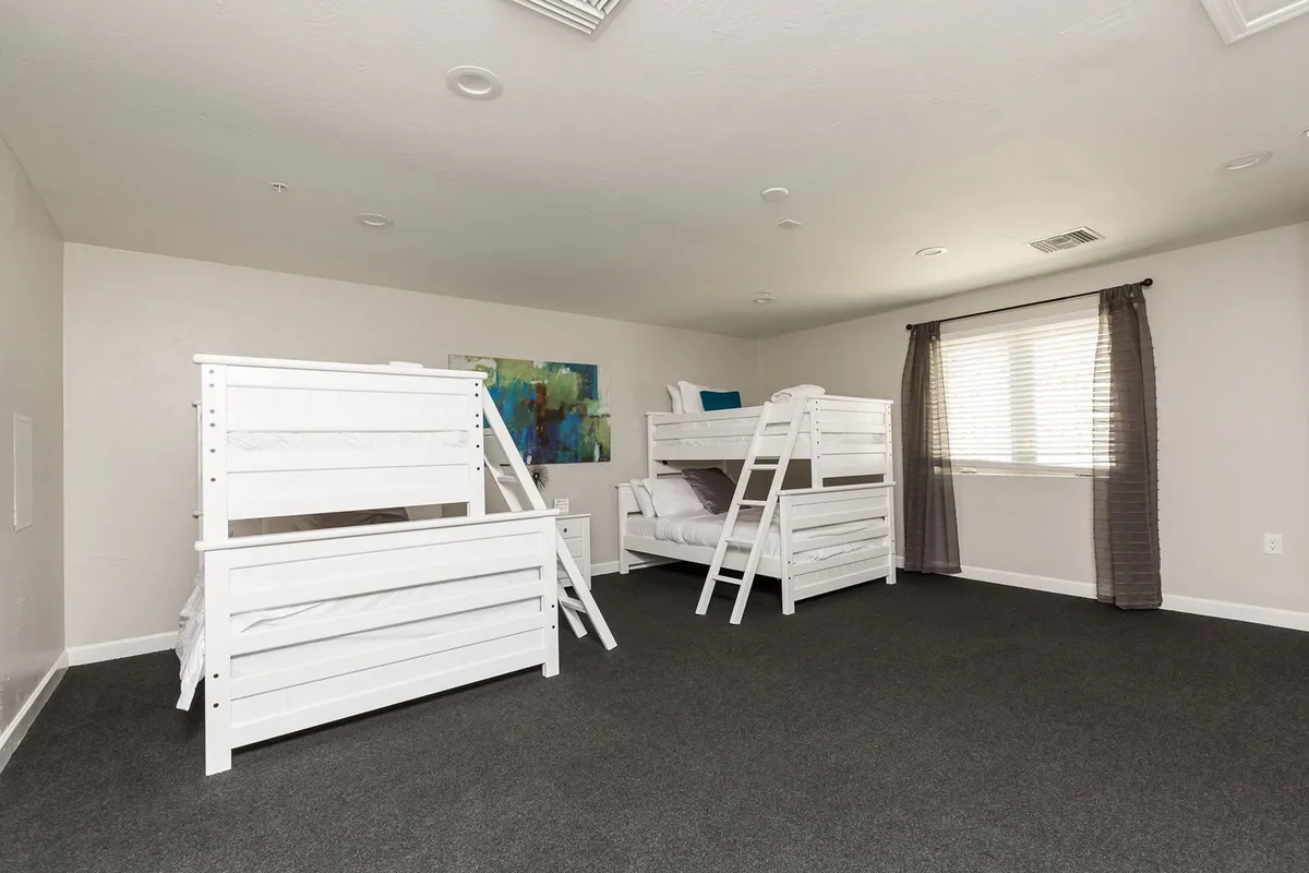 A playful bunk room with vibrant bunk beds, colorful artwork on the walls, and a window dressed with cheerful curtains. The space feels inviting and fun, ideal for kids' sleepovers and group bonding.