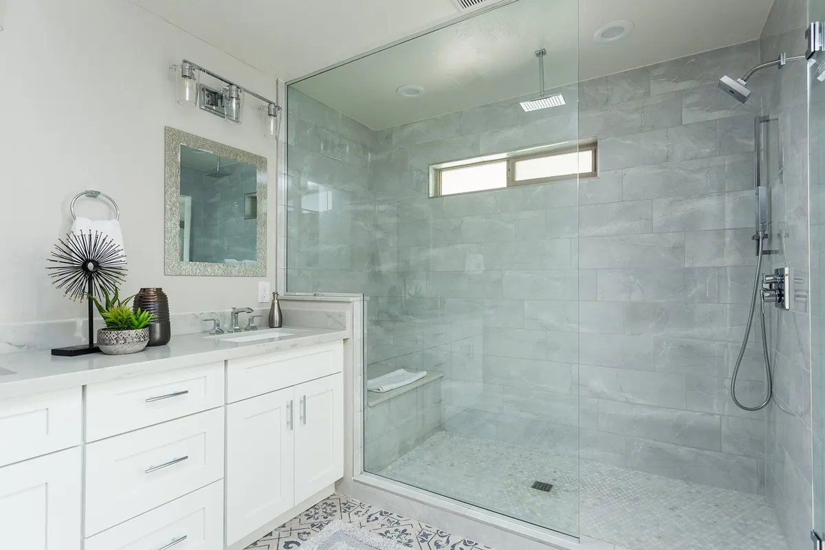 A modern bathroom featuring a sleek vanity with a vessel sink, a glass-enclosed shower, a decorative mirror, and potted plants for a touch of freshness. The space feels tranquil—perfect for self-care and rejuvenation.